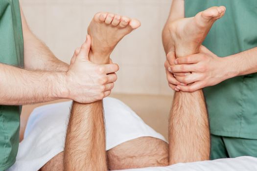 Man having leg massage on his feet by two massage therapists.