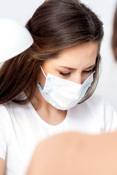 Manicurist wearing protective mask painting female nails with nail polish in manicure salon.