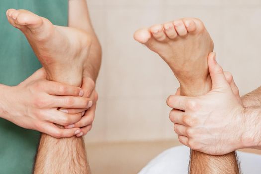 Close up of hands of two massage therapists massaging feet of man in massage salon.