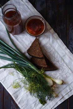 A bottle and a glass of kvass and slices of rye bread with fresh green onion and dill on white towel, traditional Russian drink, traditional folk meal concept, flat lay. selective focus