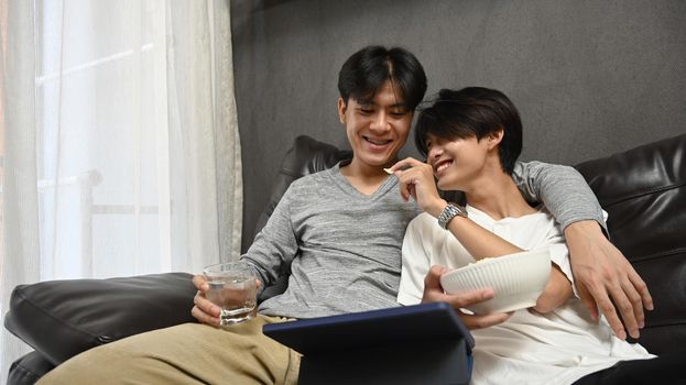 Loving same sex male couple using digital tablet together on sofa. Homosexual relationships and alternative love lifestyle concept.