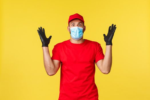 Express delivery during pandemic, covid-19, safe shipping, online shopping concept. Shocked and excited courier in uniform and medical mask, tell big news, stare impressed, yellow background.