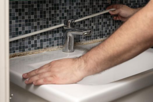 plumber removing old silicone from bathroom sink. hands close up