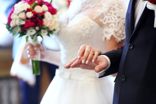 Bride and groom are holding each other's hands during church wedding ceremony