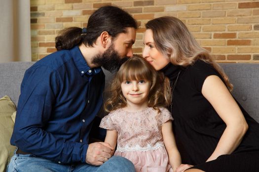 Happy young father, mother and daughter sit on wicker sofa at home. The image of a happy family expecting the second child, studio