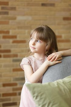 Adorable little girl looking at camera at home, smiling preschool pretty child with beautiful happy face posing alone on sofa, cute positive cheerful kid headshot portrait