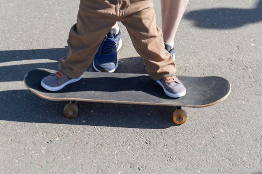 A caring and loving father teaches his three-year-old son to skateboard. A parent spends his free time with his child in the park and on a walk.