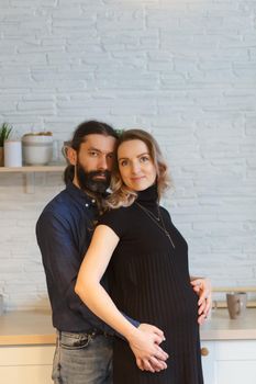 Man embracing pregnant partner in kitchen. Adult family pregnancy concept. Future parents in home outfit embrace standing in the kitchen, looking at each other. Healthy Lifestyle.