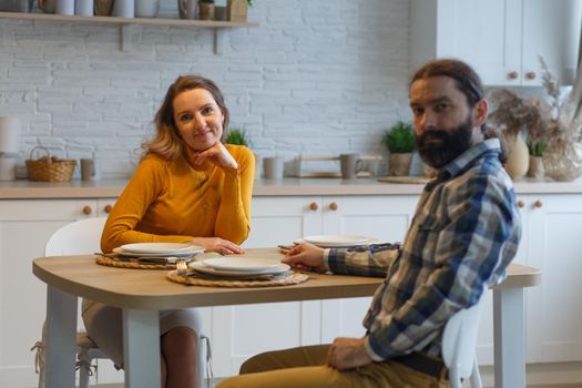 Beautiful couple having a conversation while looking at each other sitting at the table in a kitchen