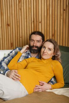 An adult couple in love waiting for a child. A man and his pregnant wife are basking in a bed in the bedroom