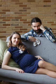 An adult couple in love waiting for a child. A man and his pregnant wife are playing on a sofa at home