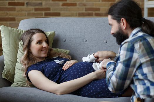 An adult couple in love waiting for a child. A man and his pregnant wife are playing on a sofa at home