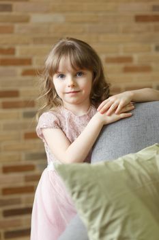 Adorable little girl looking at camera at home, smiling preschool pretty child with beautiful happy face posing alone on sofa, cute positive cheerful kid headshot portrait