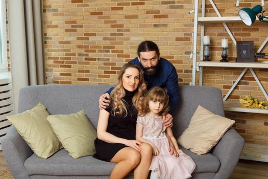 Happy young father, mother and daughter sit on wicker sofa at home. The image of a happy family expecting the second child, studio