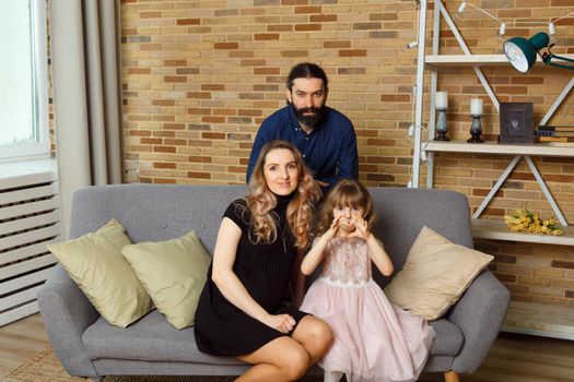 Happy young father, mother and daughter sit on wicker sofa at home. The image of a happy family expecting the second child, studio