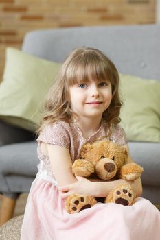 Adorable little girl with teddy bear looking at camera at home, smiling preschool pretty child with beautiful happy face posing alone on sofa, cute positive cheerful kid headshot portrait