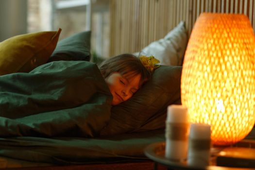 Cute little girl lying under blanket in her bed with happy face. Evening night time.