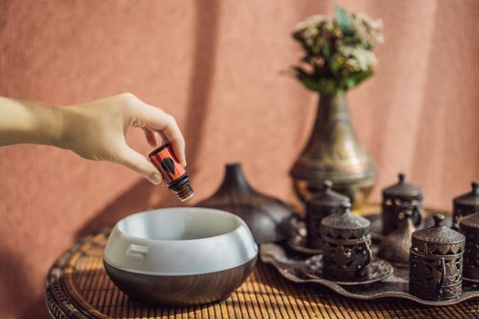 Woman adding essential oil to aroma diffuser on table.