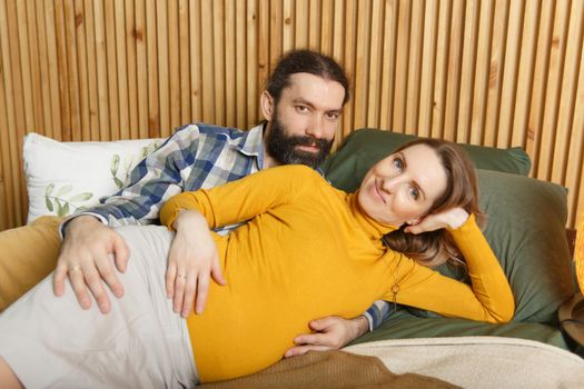 An adult couple in love waiting for a child. A man and his pregnant wife are basking in a bed in the bedroom