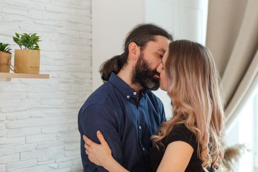 Man embracing pregnant partner in kitchen. Adult family pregnancy concept. Future parents in home outfit embrace standing in the kitchen, looking at each other, kissing. Healthy Lifestyle.