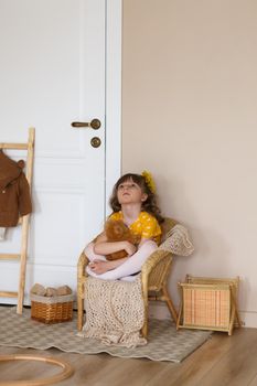 Portrait of a little upset girl in a yellow dress sitting on a chair on an abstract blue background.