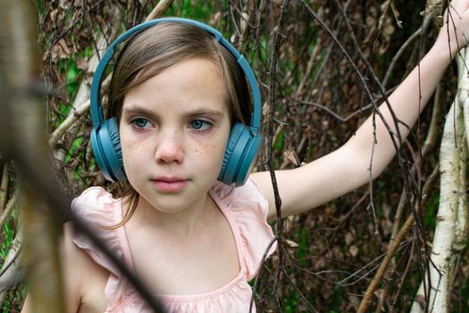 Young beautiful girl fooling around with a branch and wearing headphones on them to listen to music or block out sound due to auditory sensitivity. High quality photo