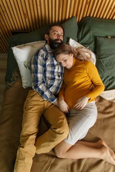 An adult couple in love waiting for a child. A man and his pregnant wife are basking in a bed in the bedroom