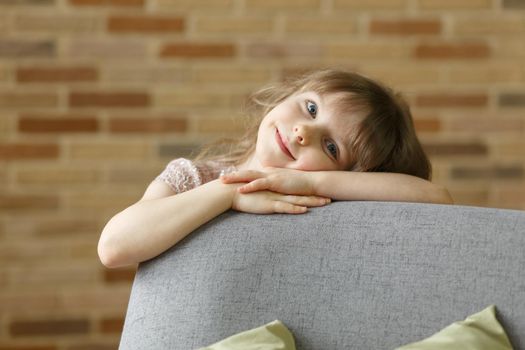 Adorable little girl looking at camera at home, smiling preschool pretty child with beautiful happy face posing alone on sofa, cute positive cheerful kid headshot portrait