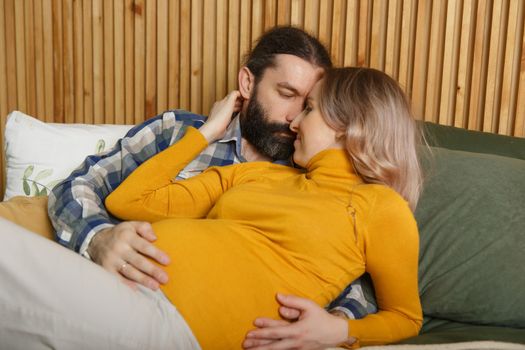 An adult couple in love waiting for a child. A man and his pregnant wife are basking in a bed in the bedroom