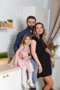 Family on the light kitchen. Pregnant woman with her husband and little daughter.