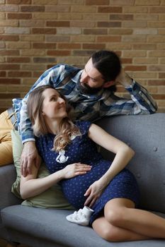 An adult couple in love waiting for a child. A man and his pregnant wife are playing on a sofa at home