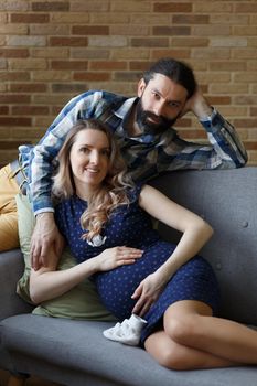 An adult couple in love waiting for a child. A man and his pregnant wife are playing on a sofa at home