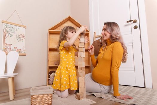 A pregnant woman plays in the nursery with her daughter. They build a tower out of wooden blocks.