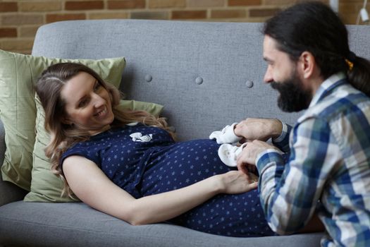 An adult couple in love waiting for a child. A man and his pregnant wife are playing on a sofa at home