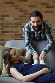 An adult couple in love waiting for a child. A man and his pregnant wife are playing on a sofa at home