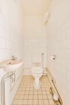 Modern flush toilet and ceramic sink installed on white tiled walls near mirror and towel in small restroom at home