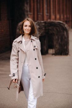 A happy stylish girl in a gray coat walks around the city.