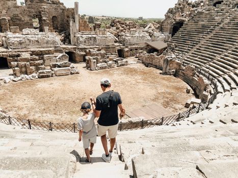 Young father dad and his school boy kid son tourists visiting ancient antique coliseum amphitheater ruins in hot summer day.