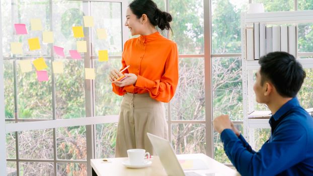 Business people work on project planning board in office and having conversation with coworker friend to analyze project development . They use sticky notes posted on glass wall to make it organized .