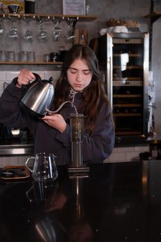 pretty brunette girl making aeropress coffee in modern coffee shop.