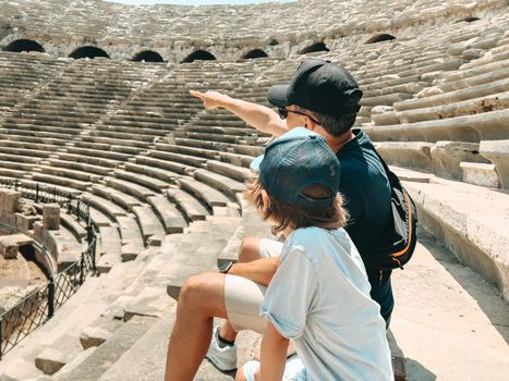 Young father dad and his school boy kid son tourists visiting ancient antique coliseum amphitheater ruins in hot summer day.