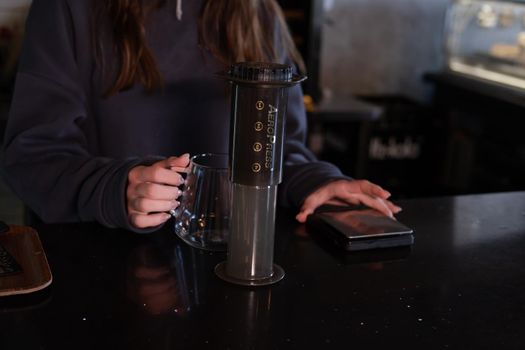 pretty brunette girl making aeropress coffee in modern coffee shop.