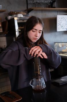 pretty brunette girl making aeropress coffee in modern coffee shop.