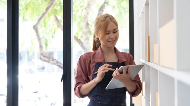 Young business woman working online e-commerce shopping at her shop. Young woman seller prepare parcel box of product for deliver to customer. Online selling, sme, e-commerce..