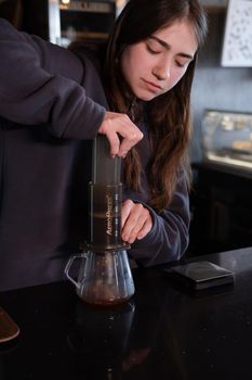 pretty brunette girl making aeropress coffee in modern coffee shop.