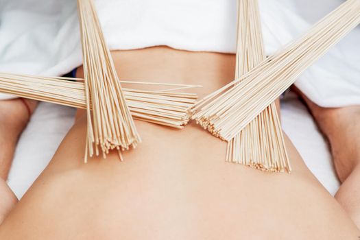 Bamboo brooms on back of young man during massage in four hands