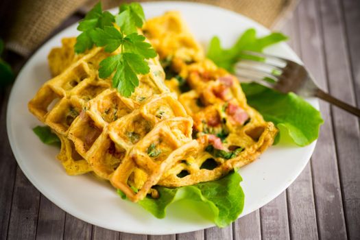 Egg omelet stuffed with greens and sausage fried in the form of waffles, on a wooden table