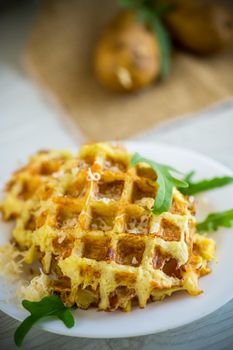 fried potato waffles with cheese in a plate on a light wooden table.