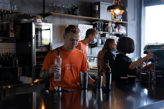 stylish young man hipster in orange t-shirt making mixing a cocktail in a dark loft cafe. alcohol drink in modern bar.