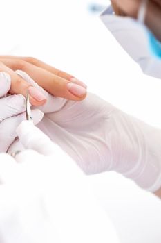 Close up of manicurist using manicure scissors to remove cuticle of female nails in manicure salon